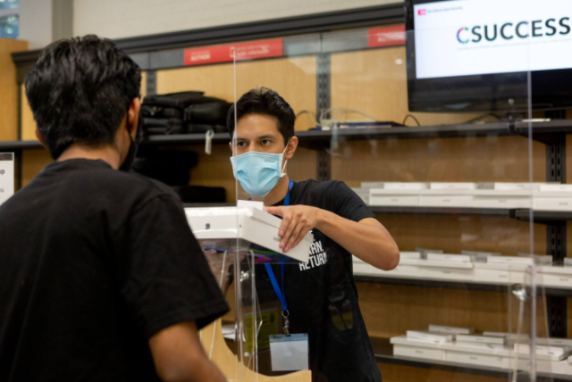 Student receiving CSUCCESS products from a man in a mask behind a clear screen.