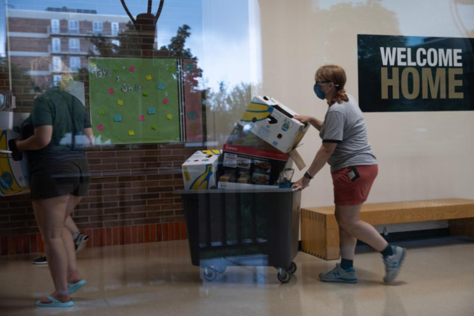 College students in a dorm during move-in day at Oakland University in Rochester, Michigan, U.S., on Friday, Aug. 27, 2021. Women moves a crate full of boxes down a hallway.