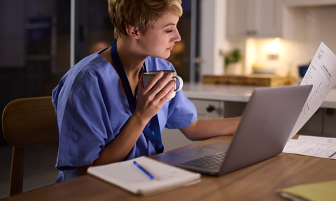 Young woman wearing medical scrubs drinking coffee and working on her coursework for an allied health program