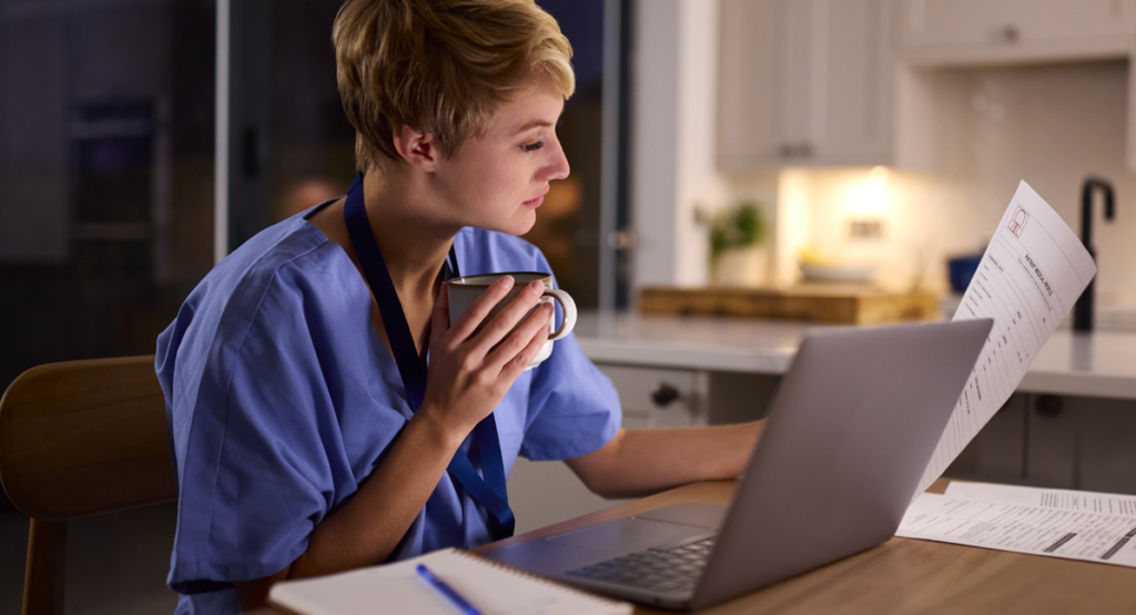 Young woman wearing medical scrubs drinking coffee and working on her coursework for an allied health program